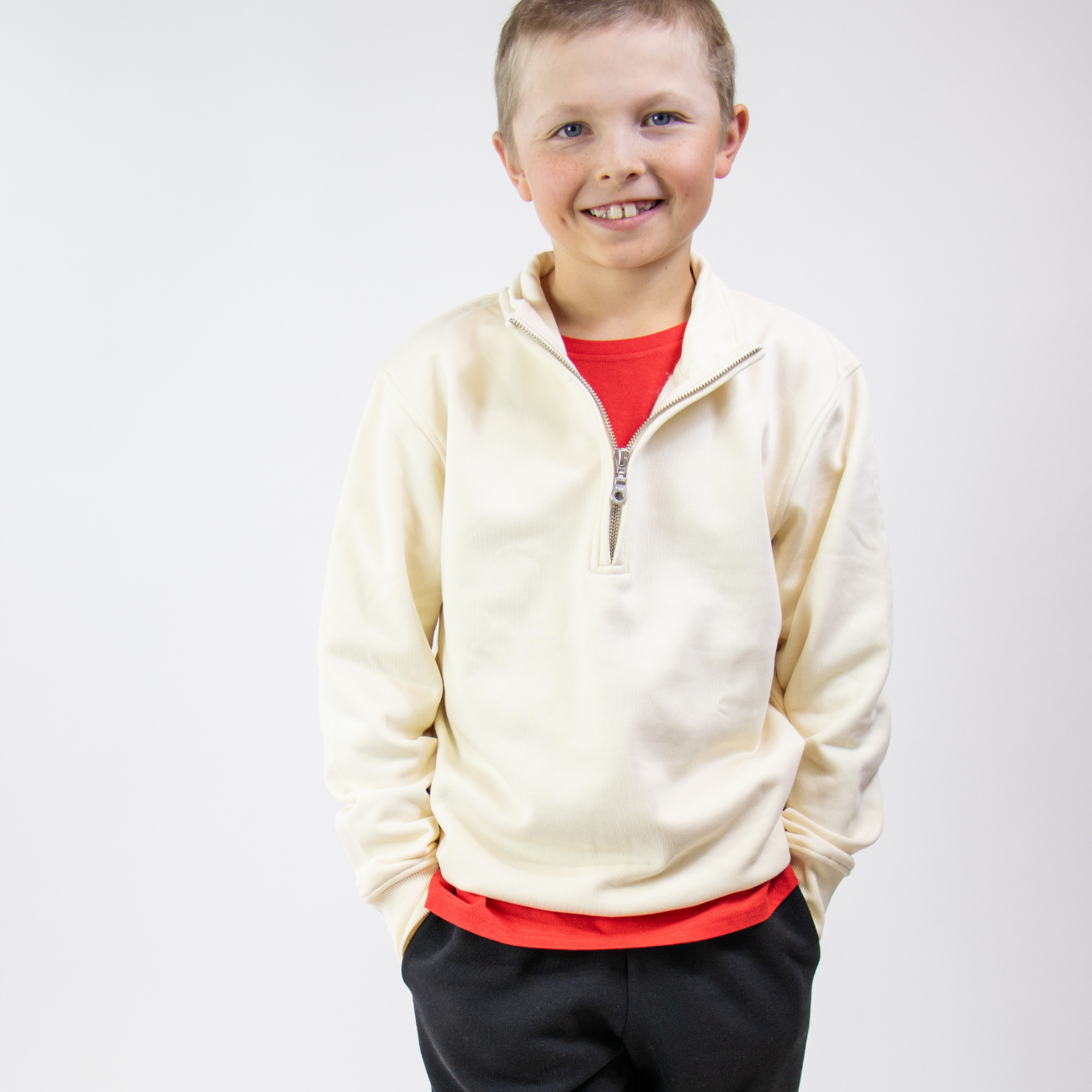 Child wearing a cream jacket over a red shirt with black pants on a white background
